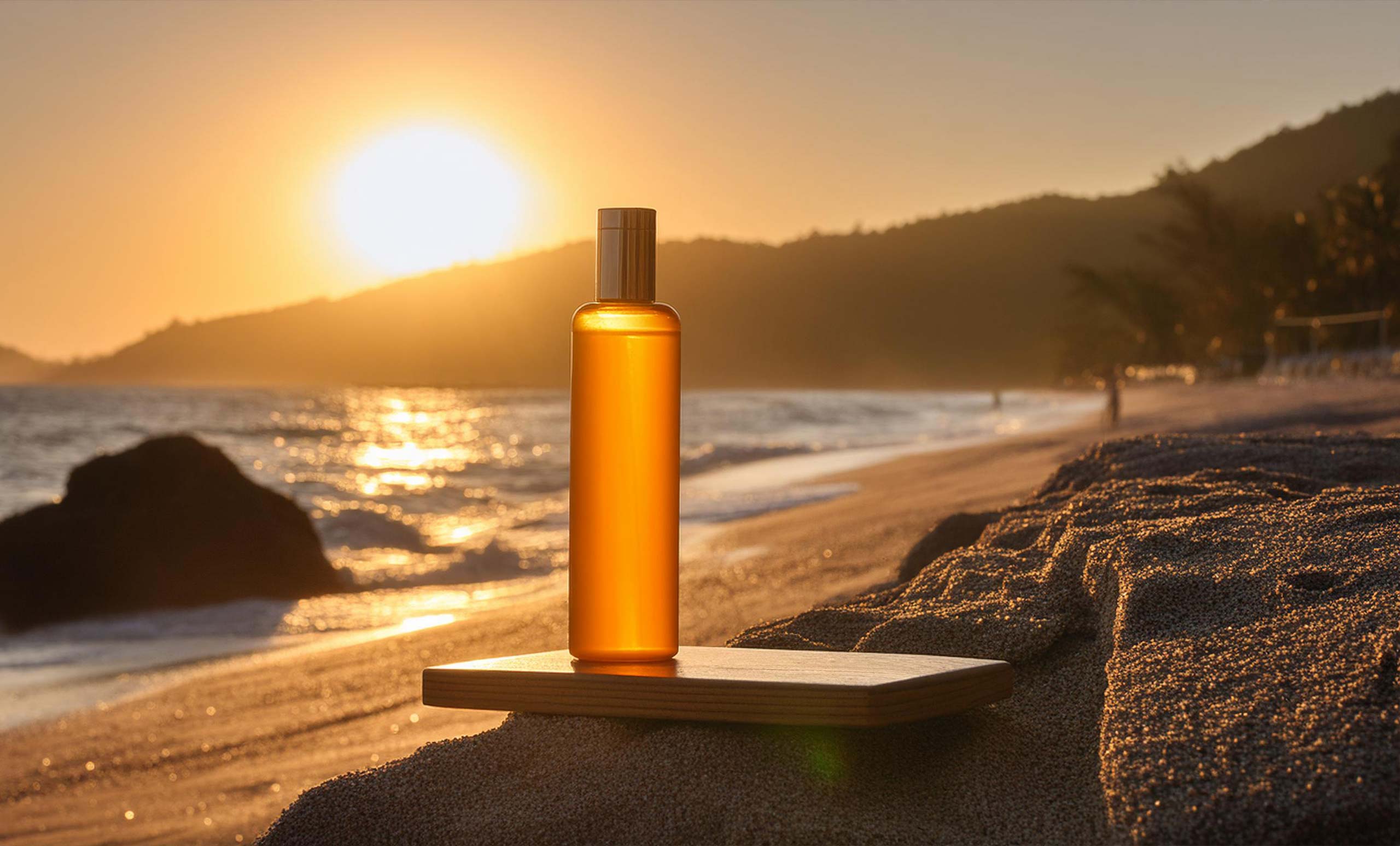 Sonnenuntergang am Strand, eine Flasche mit Sonnenschutz im Vordergrund.